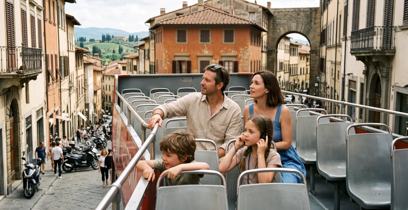 A family with two children seated on the open upper deck of a sightseeing bus traveling through a Tuscan city street.